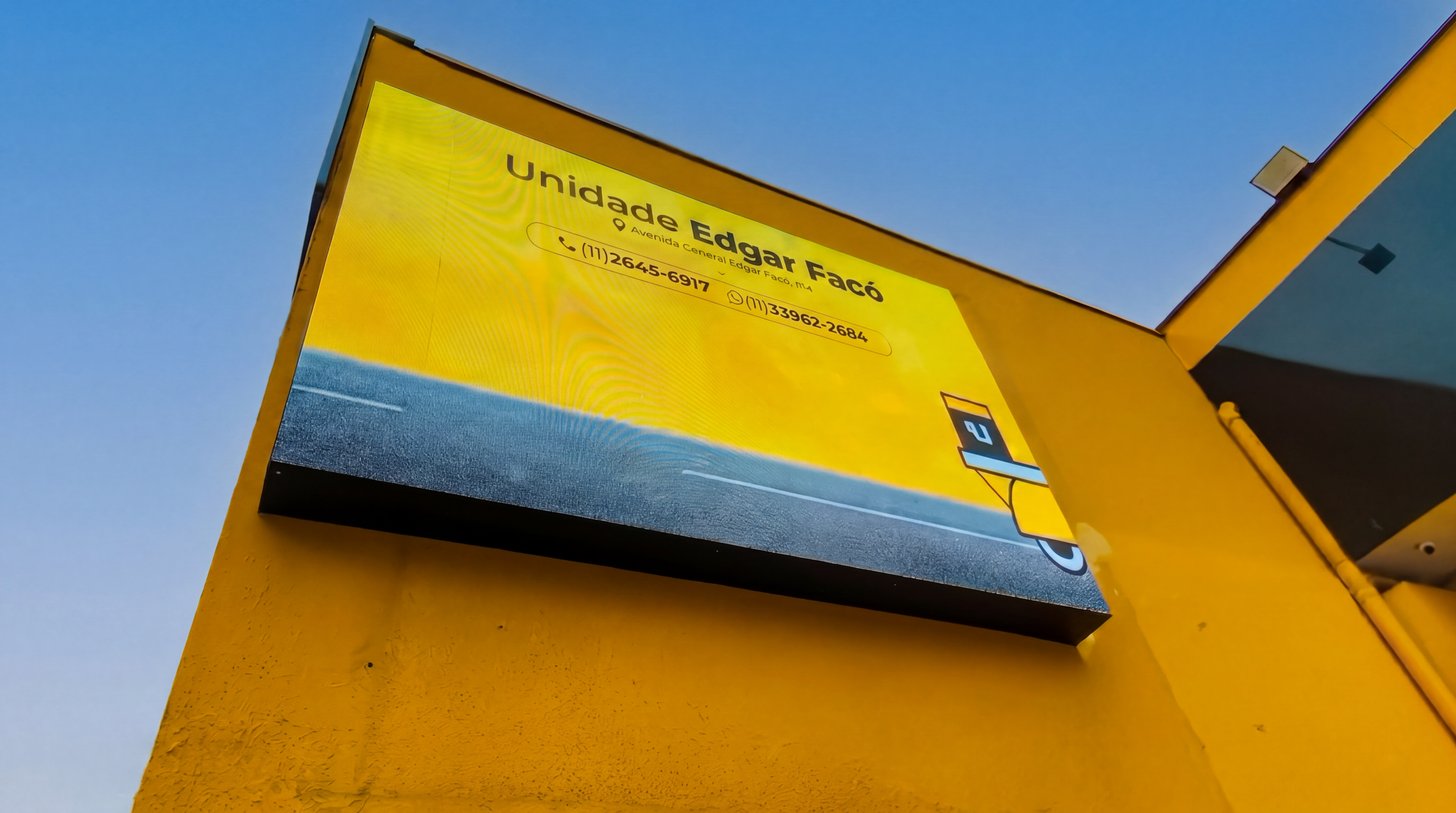 Painel P5 integrado à fachada amarela durante o dia